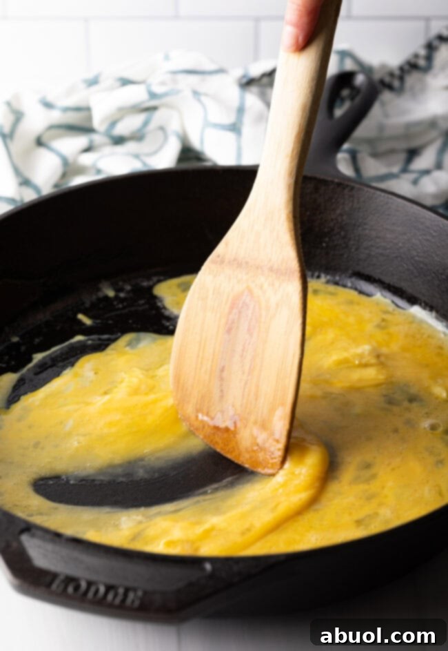Wooden spatula scrambling eggs in a cast iron skillet.