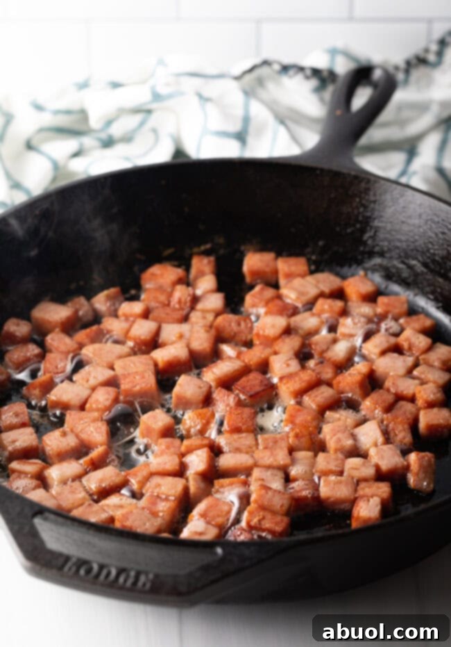 Frying cubes of spam in a cast iron skillet.