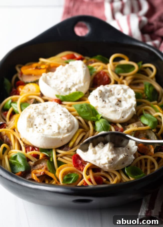 Spoon scooping creamy burrata cheese on top of spaghetti and vegetables.