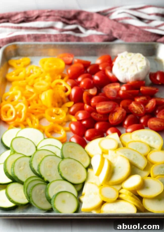 Sheet pan with piles of slices zucchini, summer squash, tomatoes, peppers, and garlic.