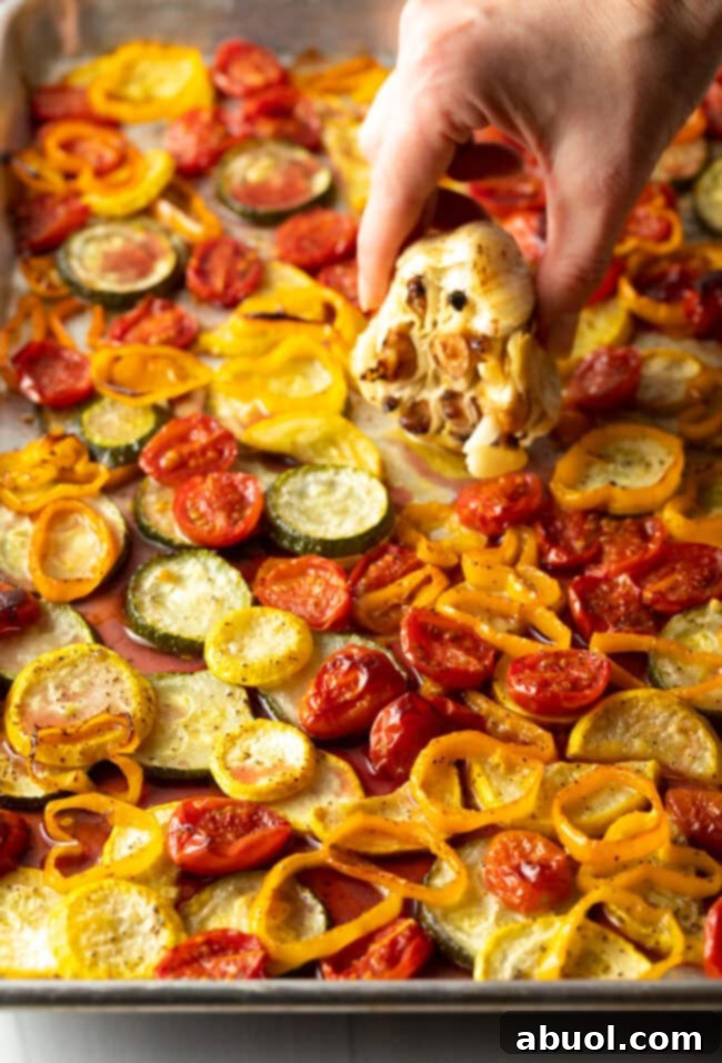 Hand squeezing out roasted garlic cloves over the pan of roasted veggies.