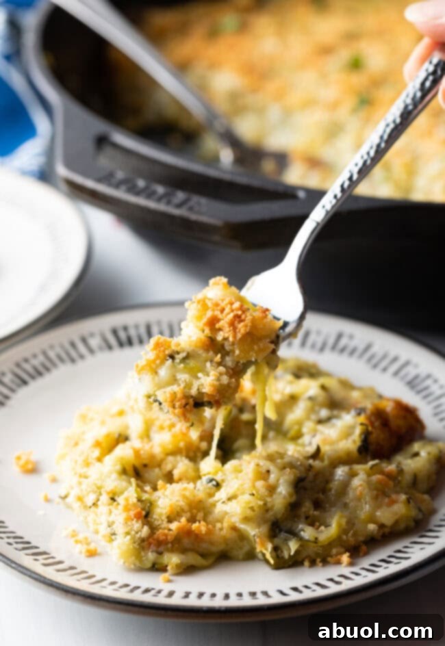 A fork holding a bite of cheesy zucchini casserole, lifted from the plate towards the camera.