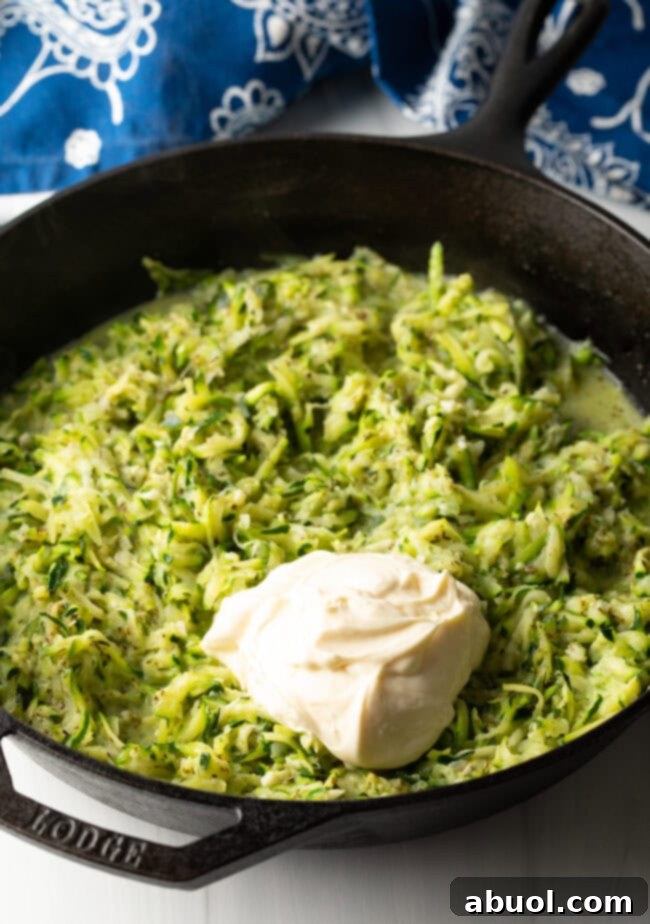 Grated zucchini in a cast iron skillet with a dollop of mayonnaise on top.