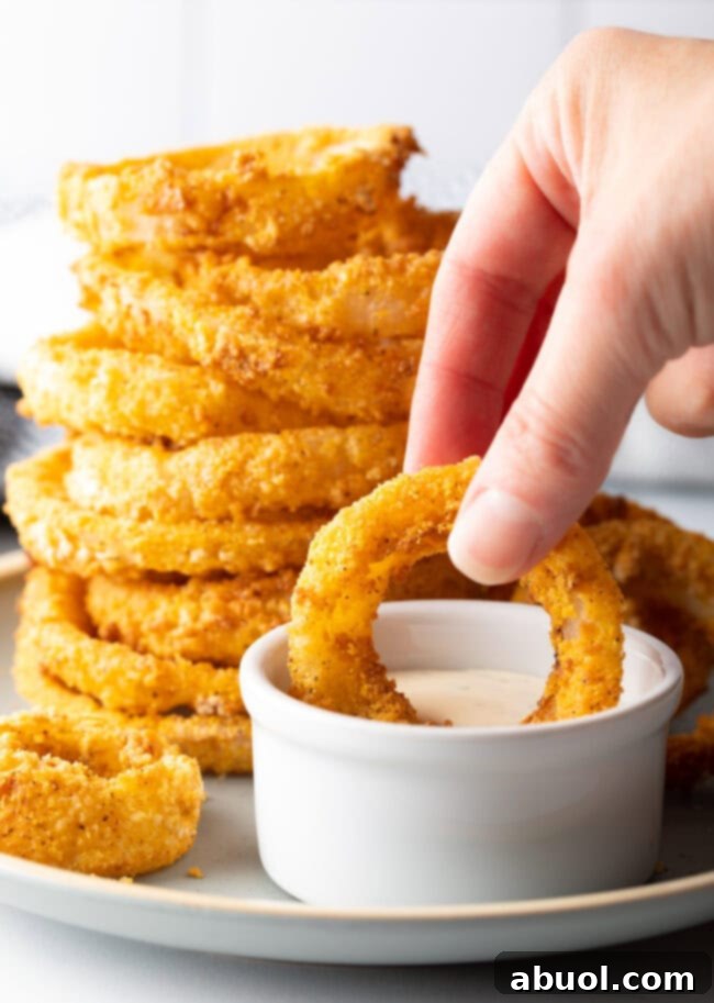 Hand dipping fried onion ring into ramekin with sauce.
