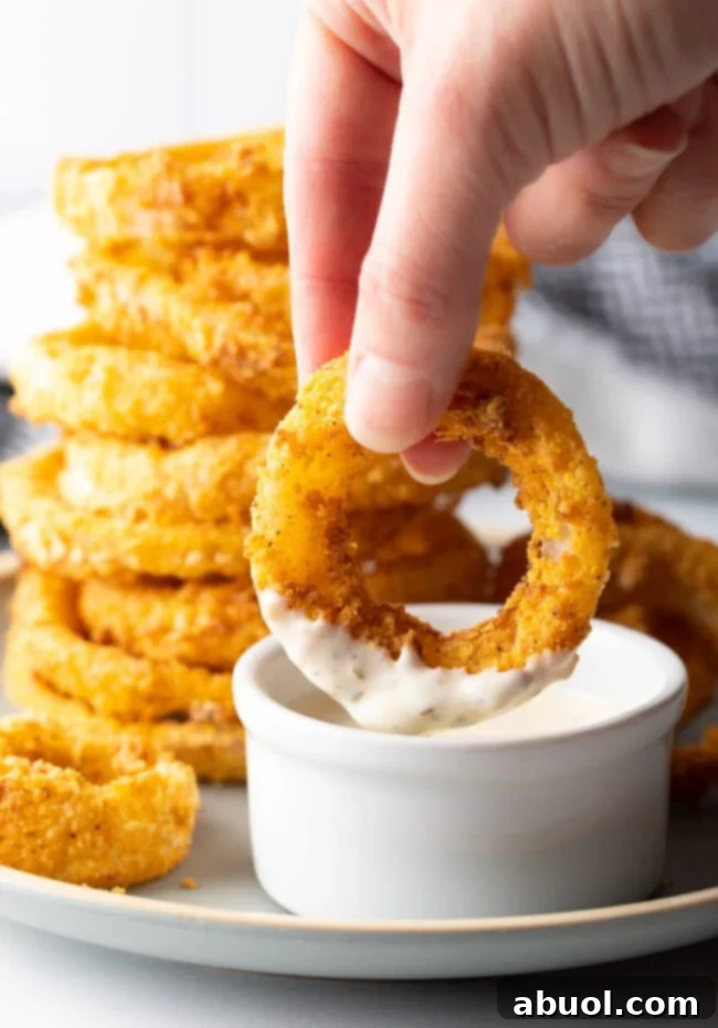 Hand dipping air fryer onion ring into sauce.