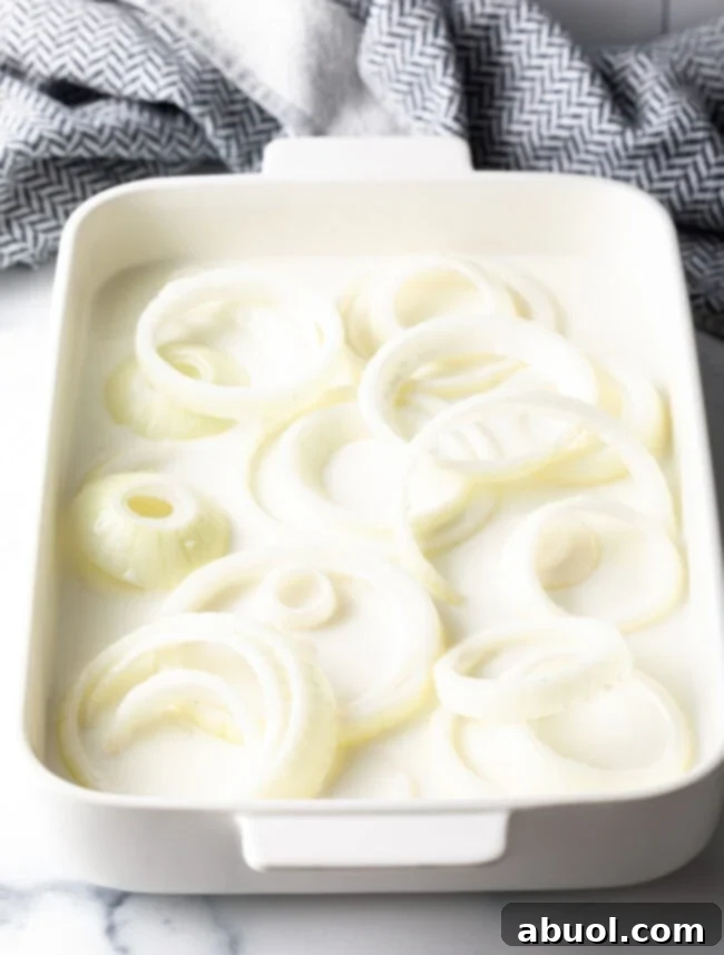 Onion rings in a baking dish soaked in buttermilk.