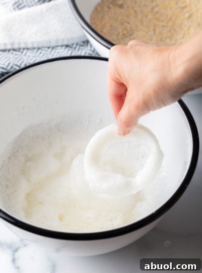 Hand dipping an onion ring into mixing bowl with whipped egg whites.