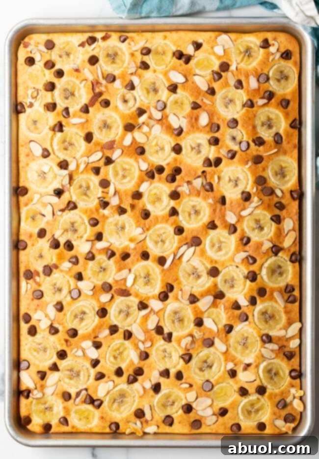 A top-down view of oven baked pancakes topped with fresh banana slices, melty chocolate chips, and toasted almond slivers, served on a white plate.
