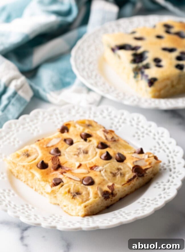 A square of chocolate chip and banana sheet pan pancake on a white plate, showcasing its fluffy texture.