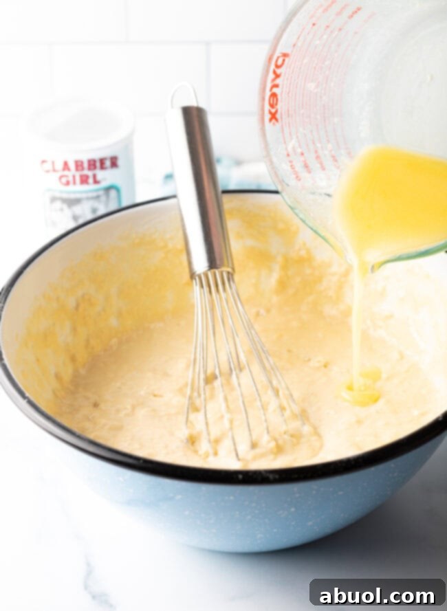 Pouring the remaining melted butter into the pancake batter in a mixing bowl, prior to final whisking.