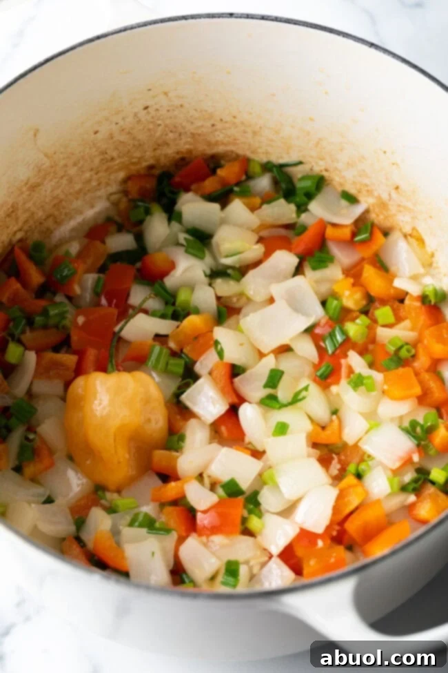 Diced peppers, onions, and a whole habanero pepper in a white cooking pot.