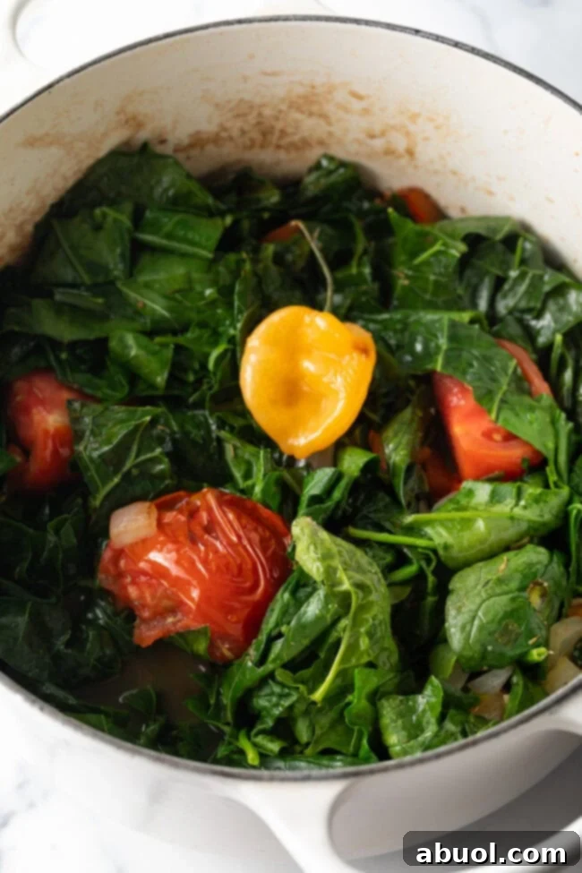 Adding fresh mixed greens to the pot with stewed tomatoes and whole habanero.
