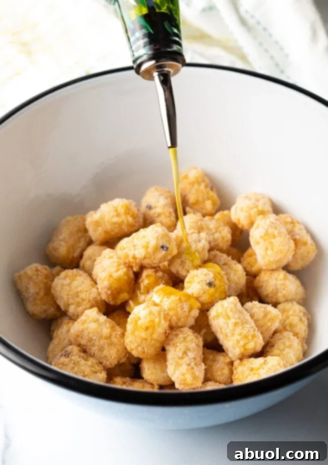 Frozen tater tots being drizzled with olive oil in a mixing bowl before seasoning.
