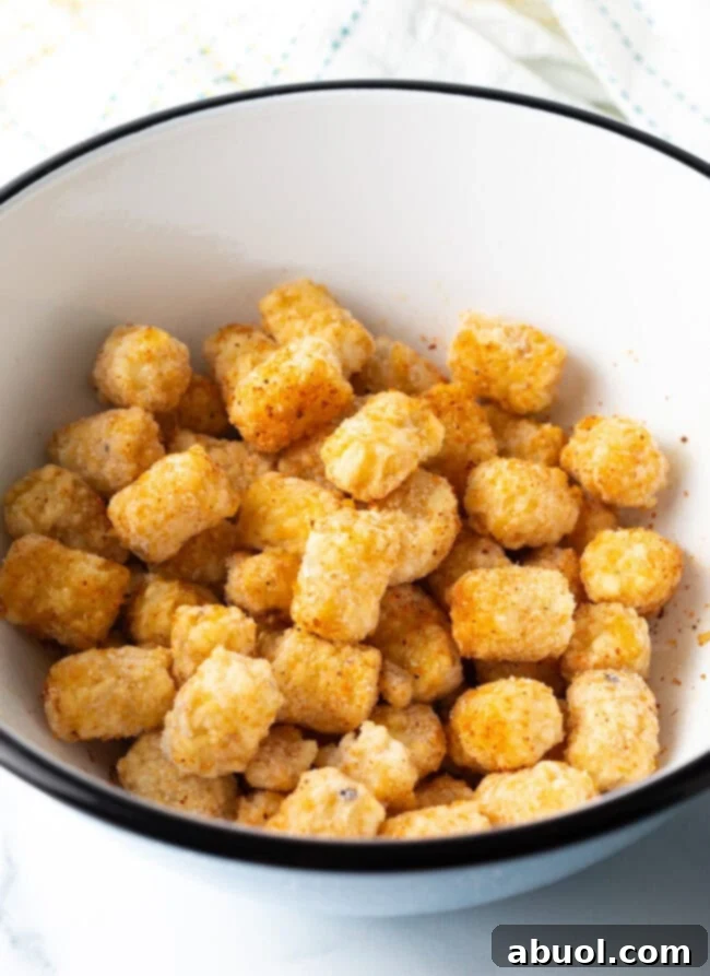 Frozen tater tots evenly coated with seasoning in a mixing bowl, ready for the air fryer.