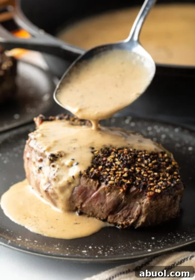Spoon pouring decadent cognac cream sauce over a perfectly seared Steak au Poivre on an elegant plate.