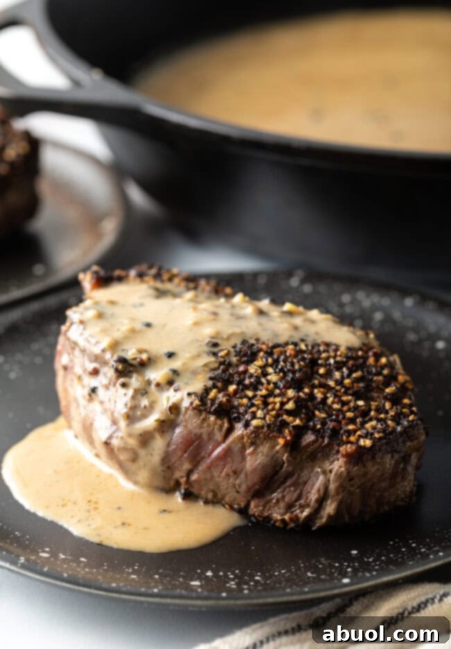 Close-up view of a perfectly seared Steak au Poivre, generously topped with creamy cognac sauce on a plate.