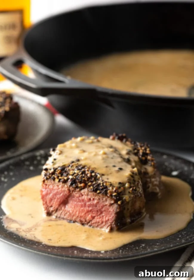 Steak au Poivre on a plate with cream sauce, a bite taken to reveal the perfect medium-rare cook inside.