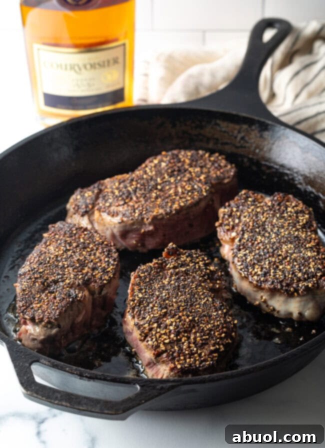 Thick pepper-crusted steaks sizzling as they are seared in a cast iron skillet, developing a golden crust.