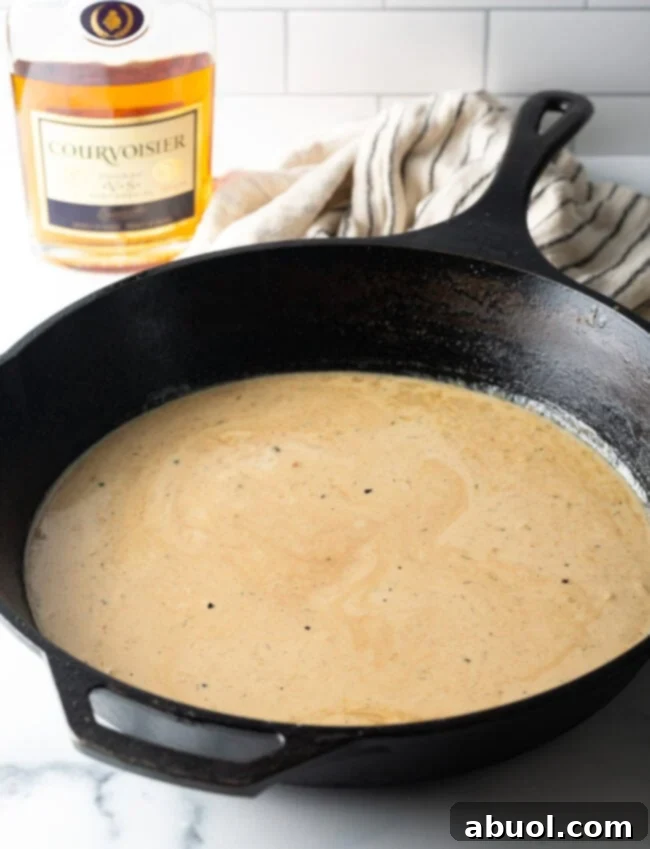 Creamy cognac sauce simmering gently in a cast iron skillet, thickening to perfection.