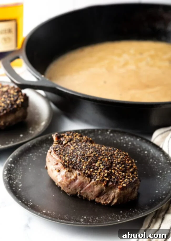 A perfectly seared and rested peppercorn steak on a white plate, ready for the sauce.