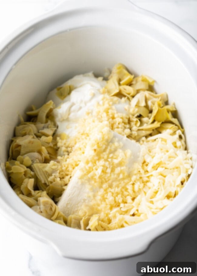 Cream cheese, parmesan cheese, minced garlic, and artichoke hearts beginning to be added to the crock pot.