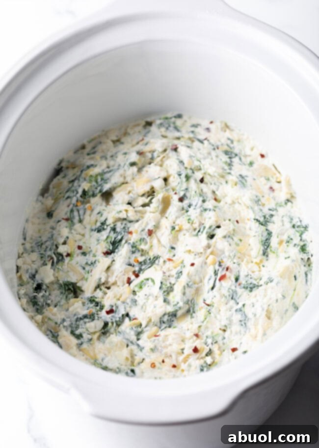 Spreading the Crockpot Spinach Artichoke Dip mixture evenly in a slow cooker before cooking.