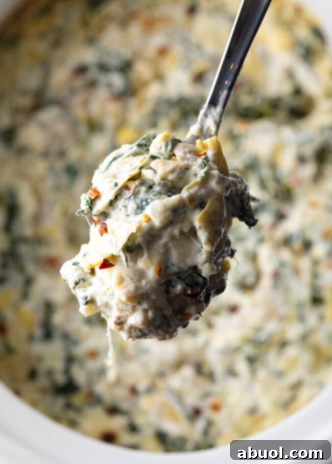 Spoon scooping warm slow cooker artichoke dip, showing its creamy texture.