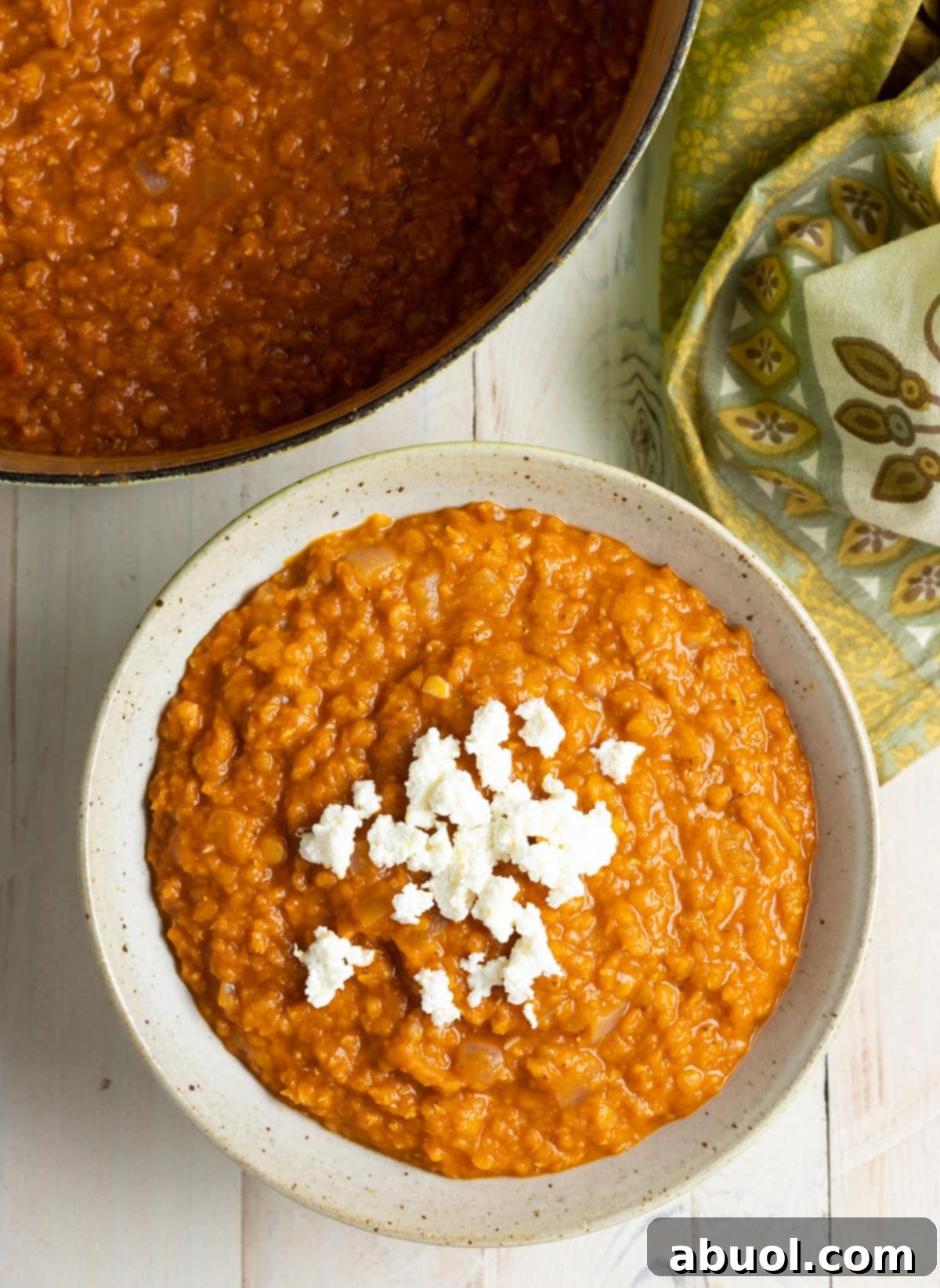 A top down view of red lentail stew in a bowl with cheese on top.