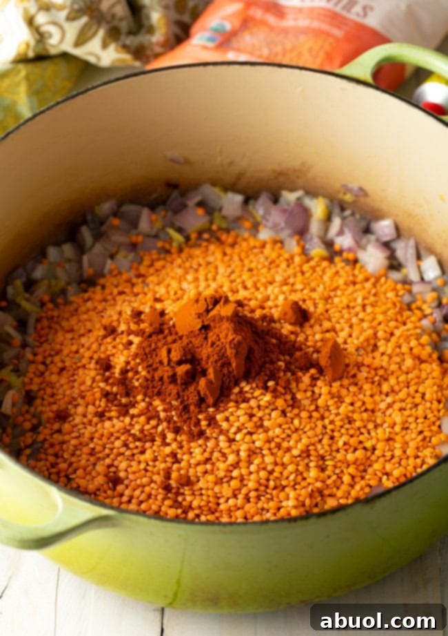Pot filled with suateed veggies and covered with uncooked lentils and spices.