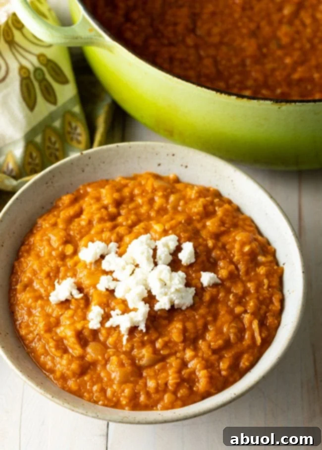 A bowl of red lentil stew with cheese on top.