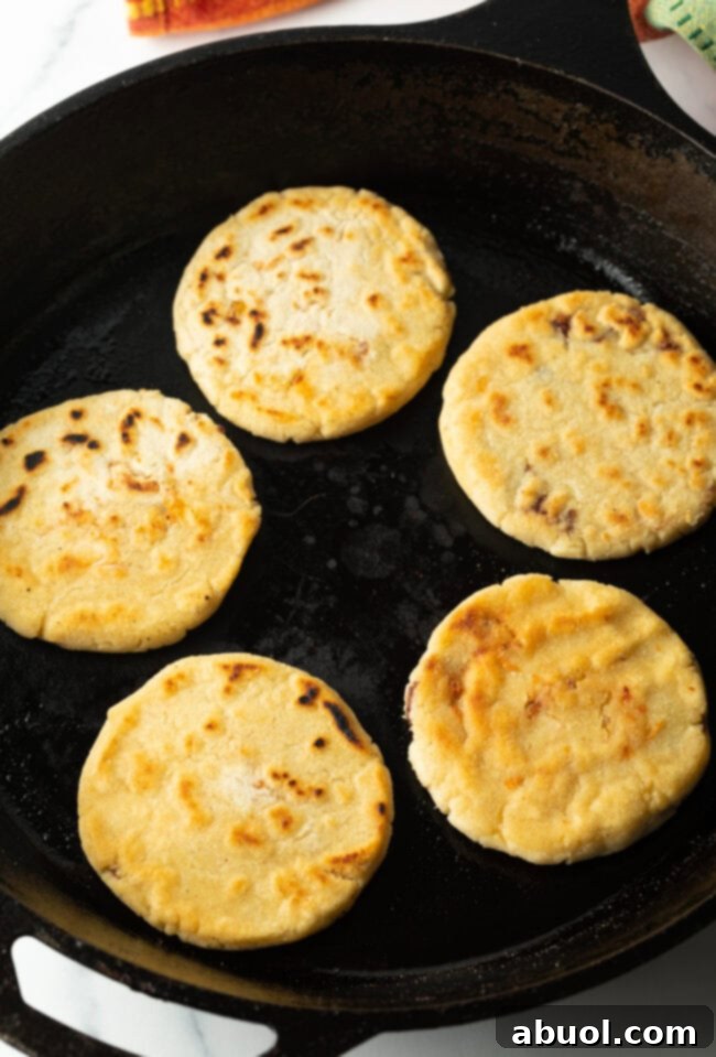 Freshly made pupusas cooking and browning to a perfect golden hue in a hot cast iron skillet.