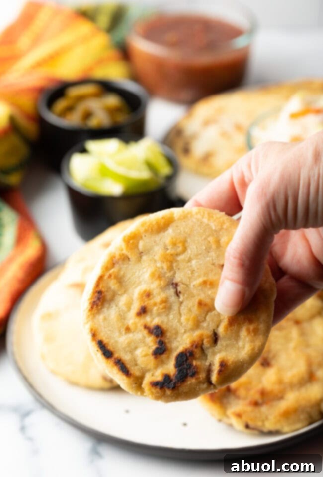 A hand holding a freshly cooked pupusa, showcasing its appetizing golden-brown exterior, ready for tasting.