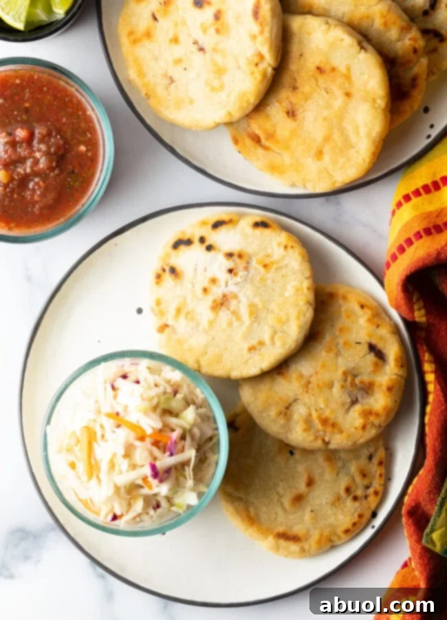 Top-down view of several pupusas on a plate, generously garnished with fresh curtido slaw, perfectly presented for a delicious meal.