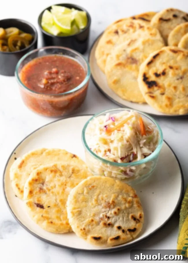 Three golden-brown pupusas artfully arranged on a clean white plate, with a small glass dish of vibrant curtido slaw presented elegantly beside them.
