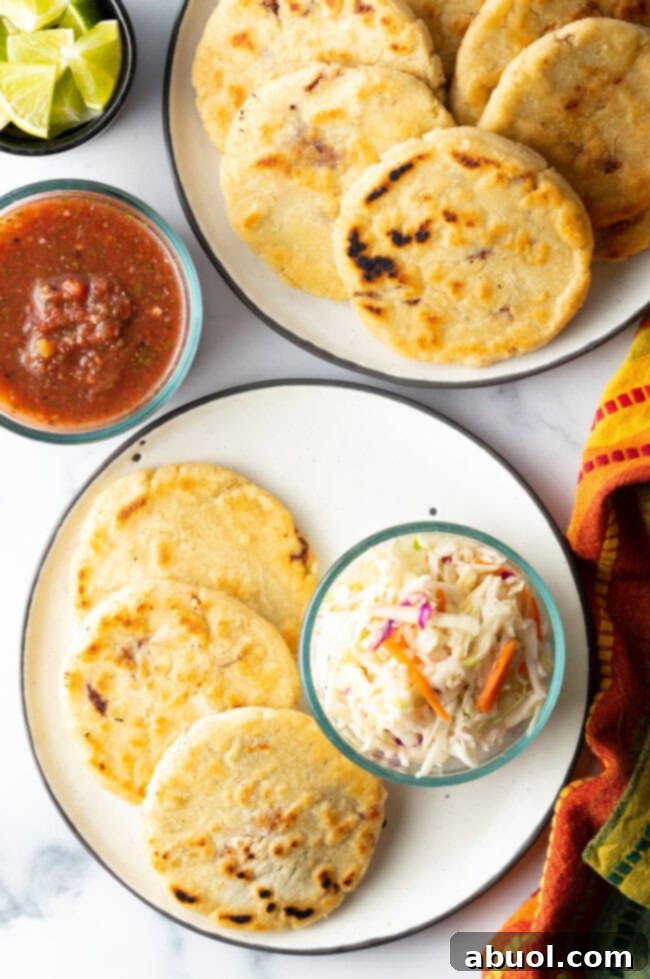 A top-down view of freshly cooked pupusas arranged on a plate, generously topped with vibrant curtido slaw.