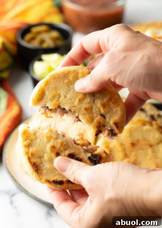 Hands tearing open a freshly cooked pupusa, revealing the luscious melted cheese and savory bean filling within.