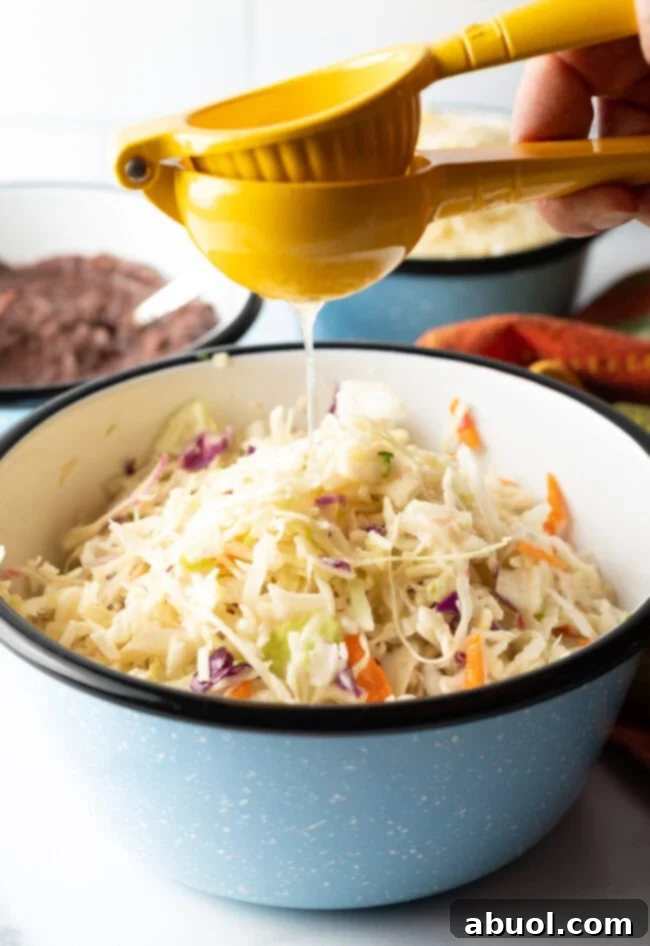 A hand squeezing fresh lime juice directly into a bowl of vibrant shredded cabbage and carrots for curtido.