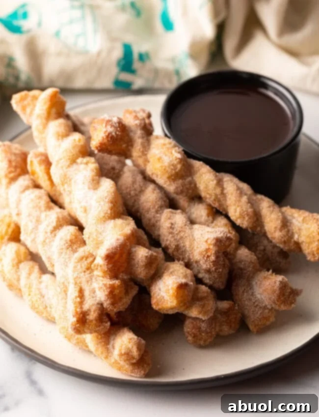 Stacked homemade cinnamon twists with a bowl of warm chocolate dipping sauce on the side, ready to be enjoyed.