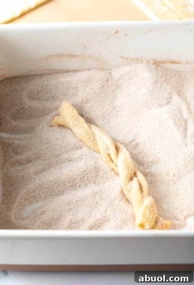Braided puff pastry twists being generously coated in a cinnamon sugar mixture.