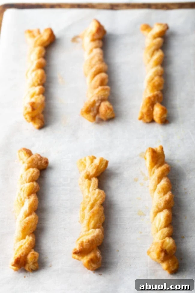 Freshly baked cinnamon twists, golden and puffy, cooling on a baking sheet.