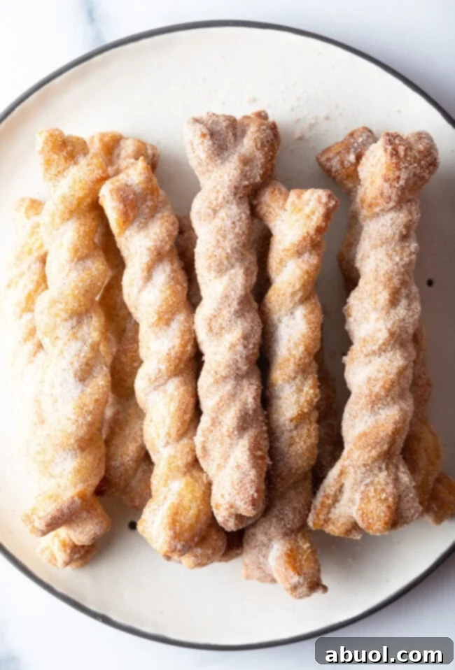Close-up top view of perfectly crisp and golden-brown cinnamon twists arranged neatly on a plate.