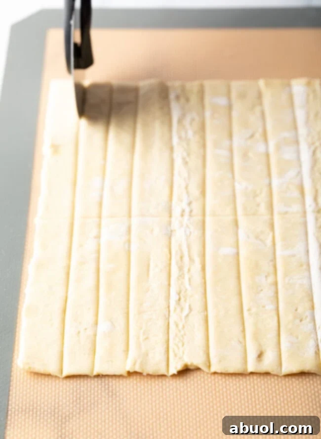 Puff pastry sheet being evenly sliced into narrow strips on a cutting board.