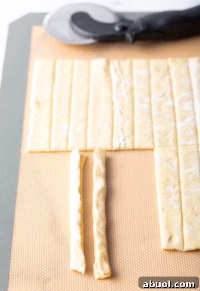 Puff pastry slivers being folded lengthwise to create thicker ribbons.