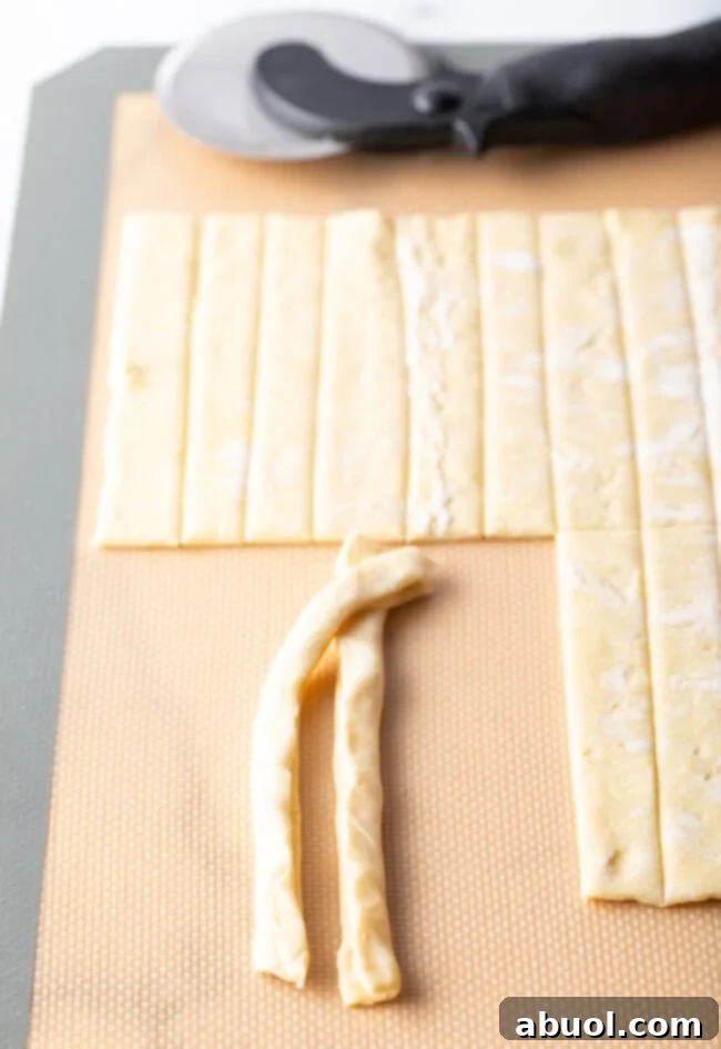 Two folded puff pastry strips being gently twisted together.