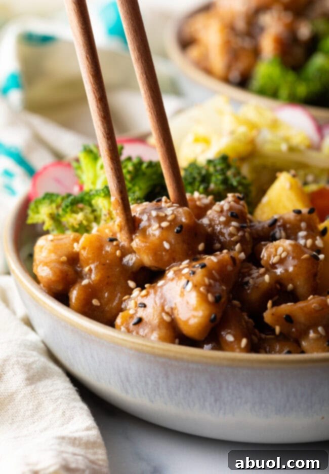 Chopsticks grabbing a piece of chicken from the bowl.