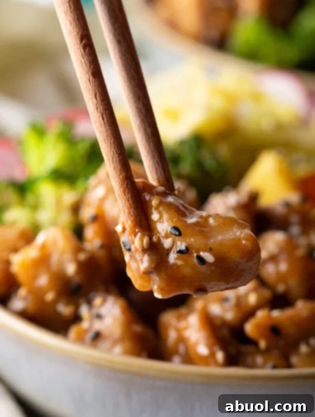 Chopsticks holding bite size piece of chicken to camera.