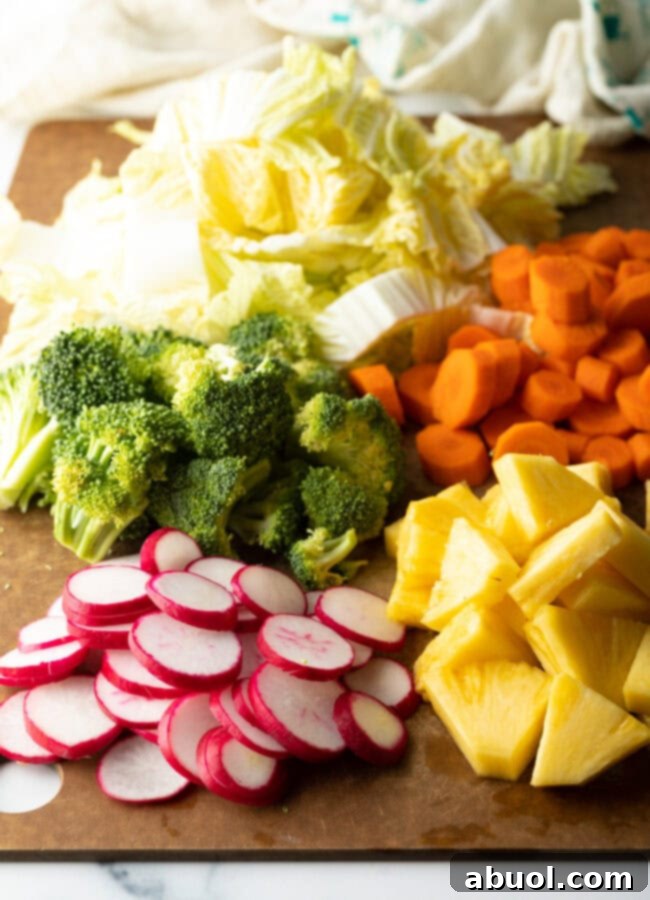 Fresh chopped veggies on a cutting board: broccoli, cabbage, carrots, pineapple, radishes.