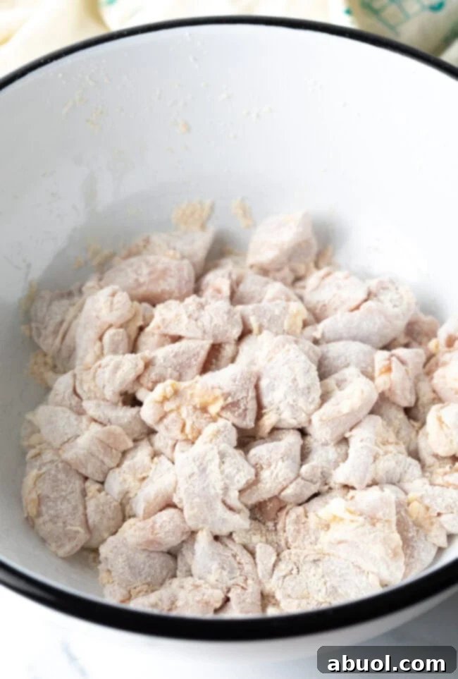 Pieces of chicken tossed with cornstarch in a bowl.