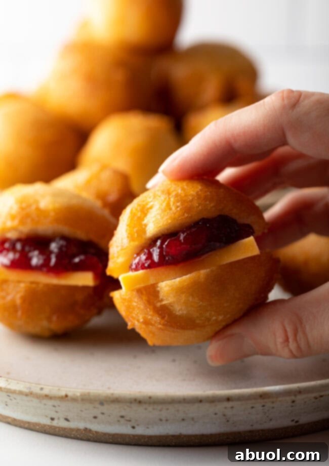Hand holding small fat cake vetkoek fried dough with cheese and jam filling.