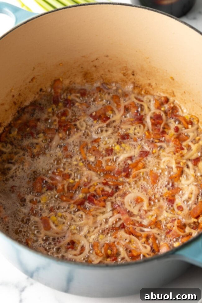 Slices of bacon and shallots gently cooking in a pot, forming the savory base of the ramen broth.